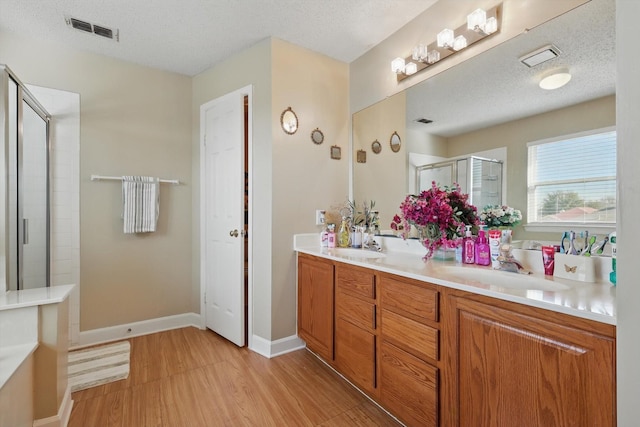 bathroom with double vanity, visible vents, a textured ceiling, and a shower stall