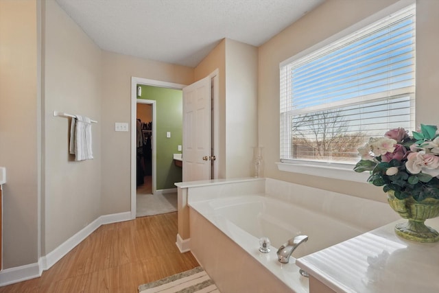 full bathroom featuring a walk in closet, a textured ceiling, wood finished floors, baseboards, and a bath