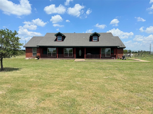 rear view of house featuring brick siding, a porch, a shingled roof, and a yard