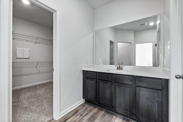 bathroom with a spacious closet, visible vents, baseboards, wood finished floors, and vanity