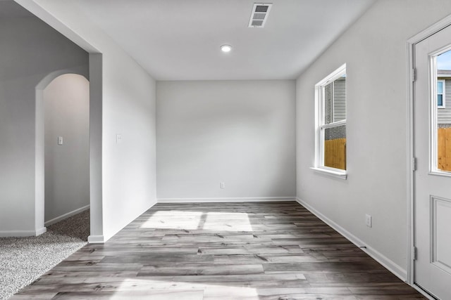 spare room with arched walkways, visible vents, baseboards, and wood finished floors