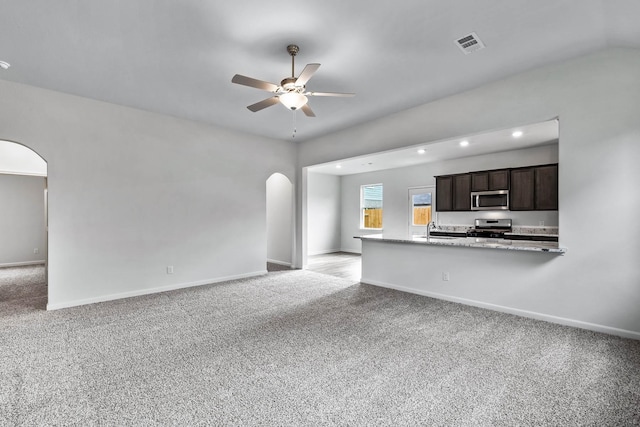 unfurnished living room with a ceiling fan, baseboards, visible vents, arched walkways, and light carpet