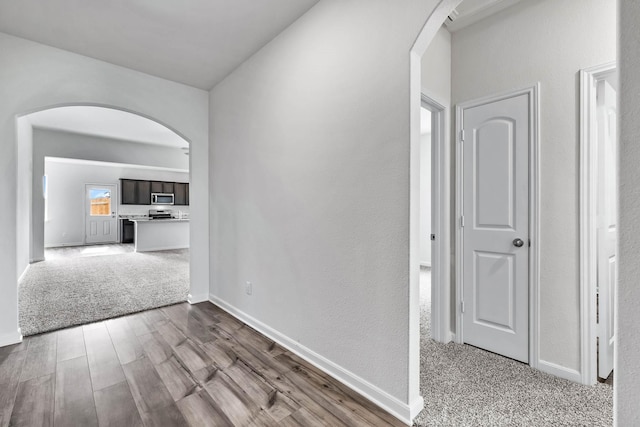 hallway with carpet, wood finished floors, baseboards, and arched walkways