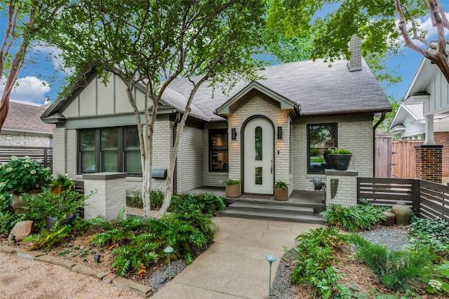 english style home with brick siding, a chimney, and fence