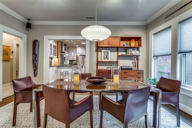 dining space with visible vents, light wood-type flooring, crown molding, and baseboards