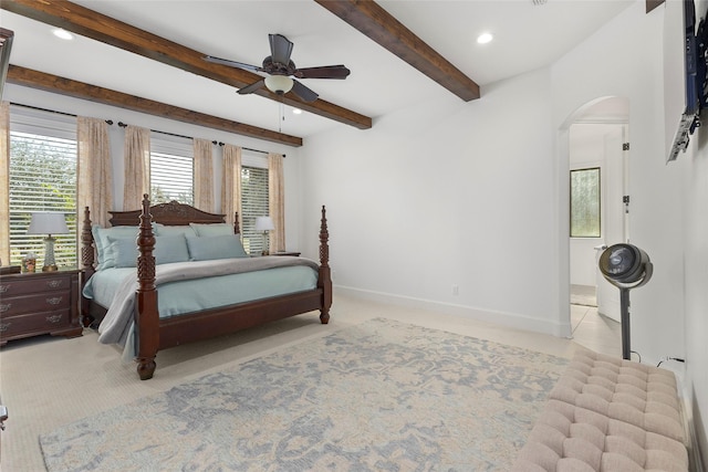 carpeted bedroom featuring baseboards, beam ceiling, recessed lighting, ensuite bathroom, and arched walkways