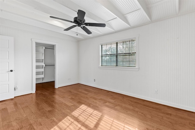 unfurnished bedroom featuring a walk in closet, beam ceiling, light wood-style flooring, baseboards, and ceiling fan