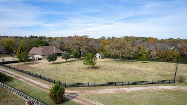 view of community with a rural view, a view of trees, a yard, and fence