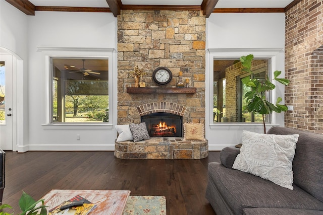 living room featuring baseboards, ornamental molding, a stone fireplace, hardwood / wood-style flooring, and beamed ceiling