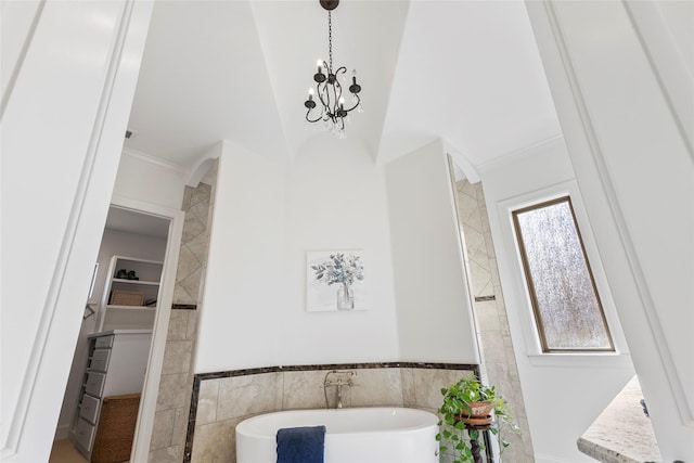 bathroom featuring crown molding, a walk in closet, an inviting chandelier, a soaking tub, and tile walls