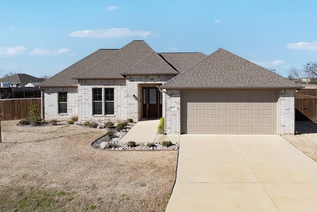 french provincial home with brick siding, driveway, a shingled roof, and fence