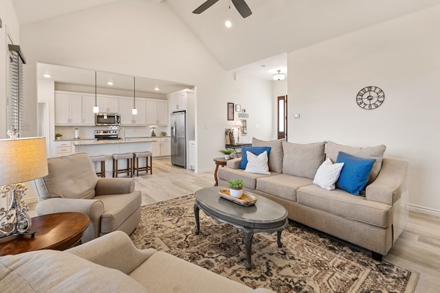 living room featuring baseboards, high vaulted ceiling, light wood-type flooring, and a ceiling fan