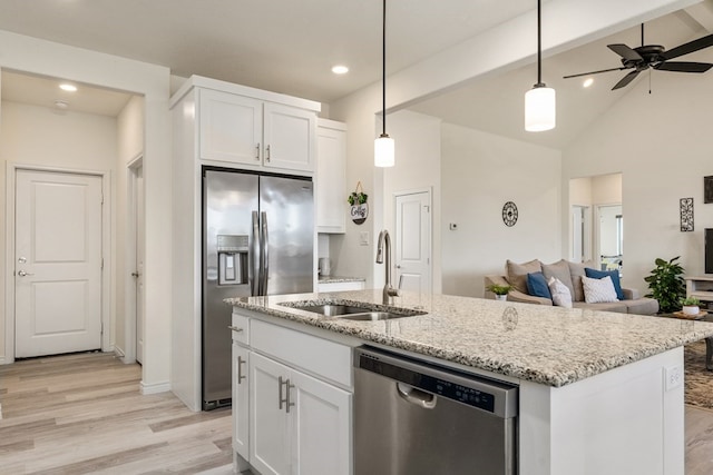 kitchen with light stone counters, a sink, stainless steel appliances, white cabinetry, and open floor plan