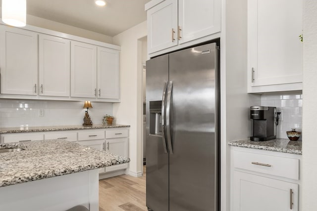 kitchen with backsplash, light wood-type flooring, light stone counters, white cabinets, and stainless steel fridge