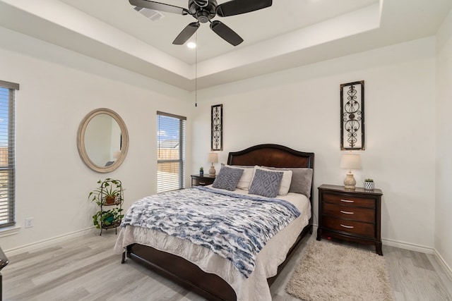 bedroom featuring a tray ceiling, baseboards, a ceiling fan, and light wood finished floors