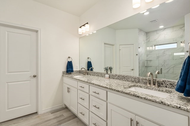 full bath with wood finished floors, visible vents, a marble finish shower, double vanity, and a sink