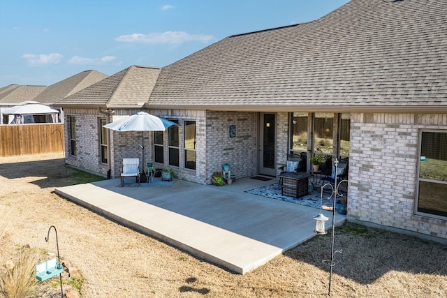 exterior space with a patio area, brick siding, roof with shingles, and fence