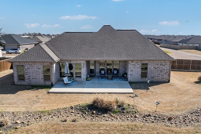 rear view of house featuring a patio, brick siding, fence, and a shingled roof