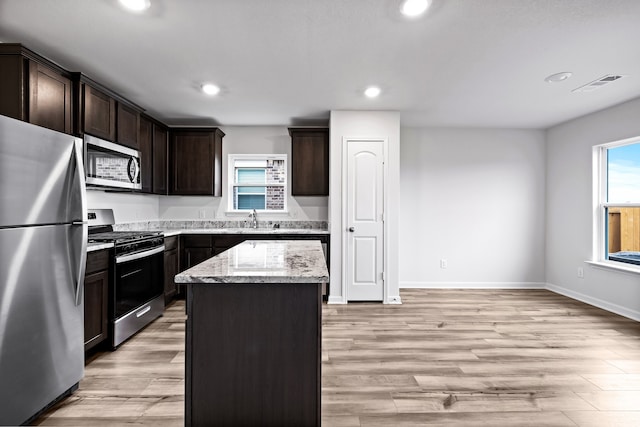 kitchen with light stone countertops, visible vents, a sink, stainless steel appliances, and light wood-type flooring