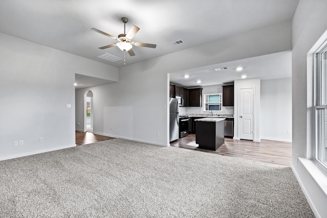 unfurnished living room featuring arched walkways, visible vents, a ceiling fan, and carpet floors