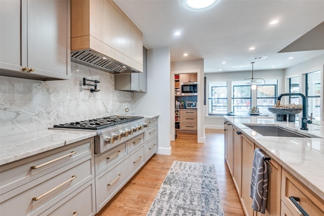 kitchen with a sink, light wood-style floors, appliances with stainless steel finishes, light stone countertops, and custom exhaust hood