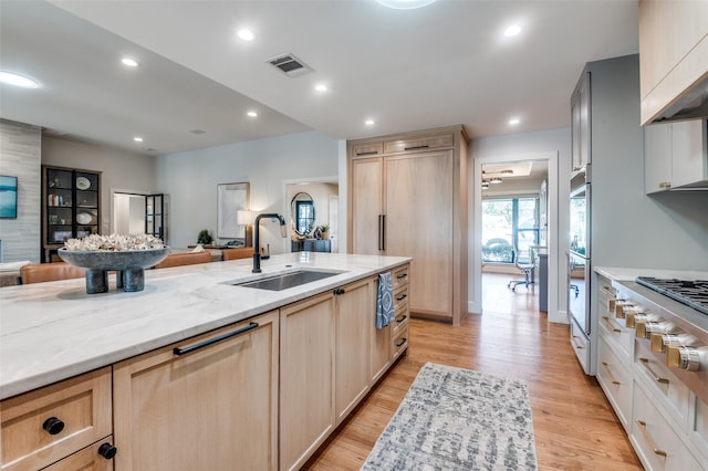 kitchen with a sink, visible vents, light stone counters, and light brown cabinetry