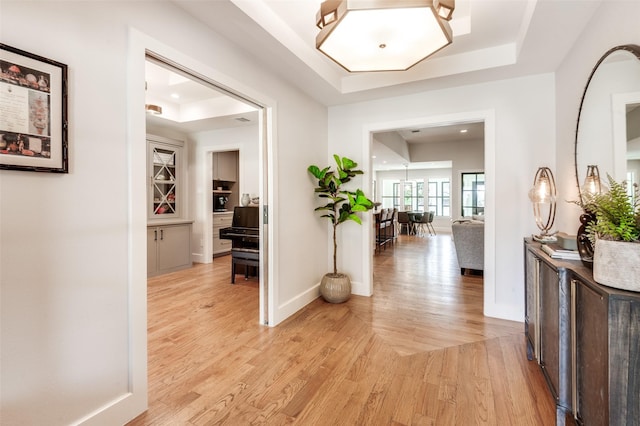 hall with recessed lighting, baseboards, a raised ceiling, and light wood-style floors