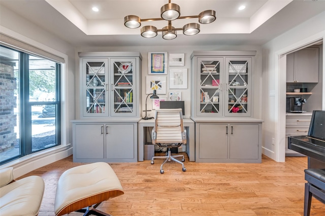 office featuring a raised ceiling, a notable chandelier, recessed lighting, and light wood-type flooring