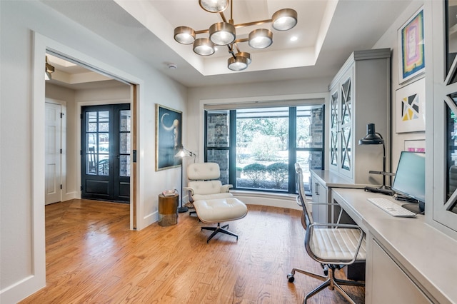 home office featuring a wealth of natural light, baseboards, a raised ceiling, and light wood finished floors