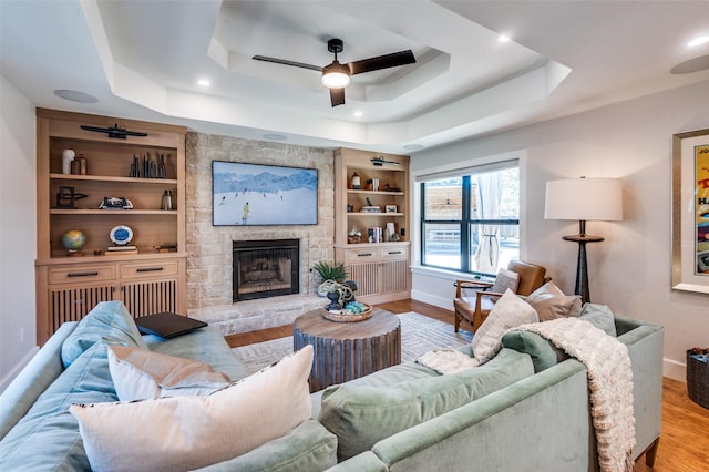 living room featuring built in features, wood finished floors, baseboards, a tray ceiling, and a fireplace