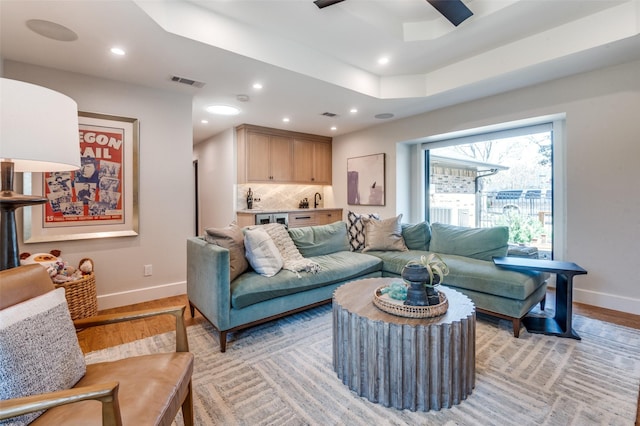 living area with recessed lighting, visible vents, a raised ceiling, and light wood-style flooring