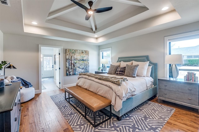 bedroom featuring a raised ceiling, multiple windows, and wood finished floors