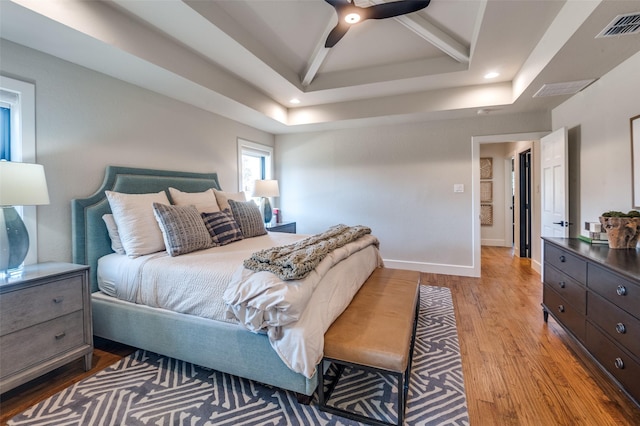 bedroom featuring visible vents, light wood-style flooring, a tray ceiling, recessed lighting, and baseboards