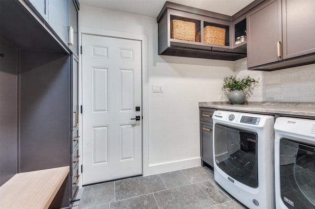 clothes washing area with washing machine and clothes dryer, cabinet space, stone finish floor, and baseboards