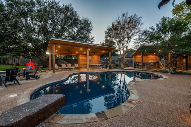 view of pool with a ceiling fan, a patio area, a fenced backyard, and an outdoor kitchen