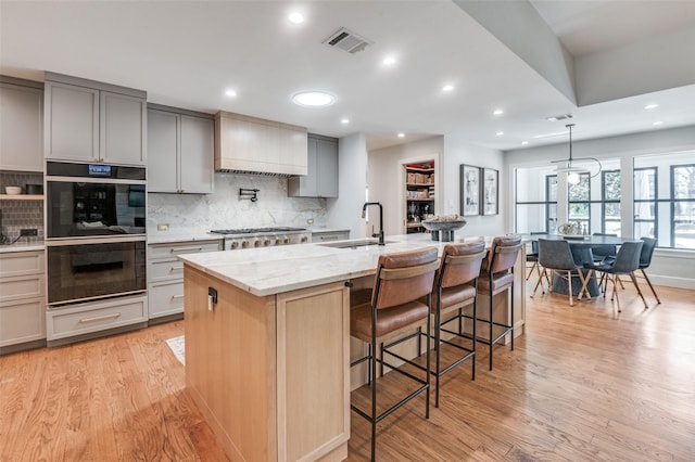 kitchen featuring visible vents, stainless steel gas cooktop, double oven, gray cabinets, and a sink