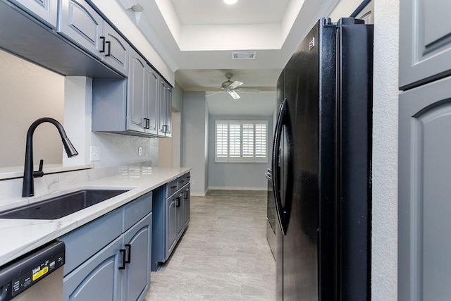 kitchen featuring a ceiling fan, freestanding refrigerator, a sink, dishwasher, and a raised ceiling