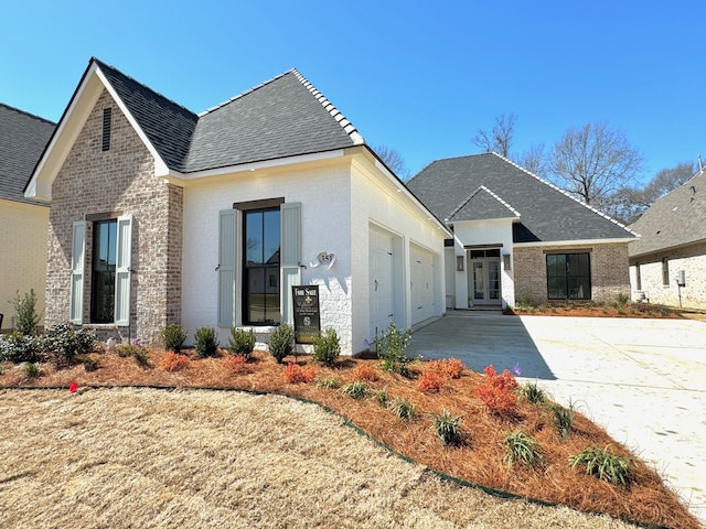 view of front of property featuring brick siding, an attached garage, concrete driveway, and french doors