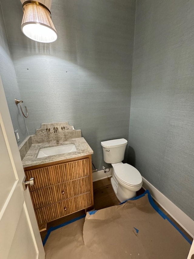 half bathroom featuring baseboards, toilet, and vanity