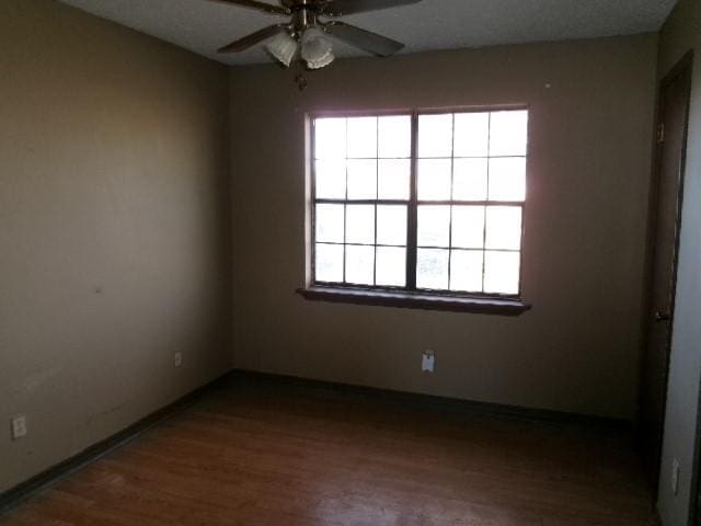 spare room featuring baseboards, wood finished floors, and a ceiling fan