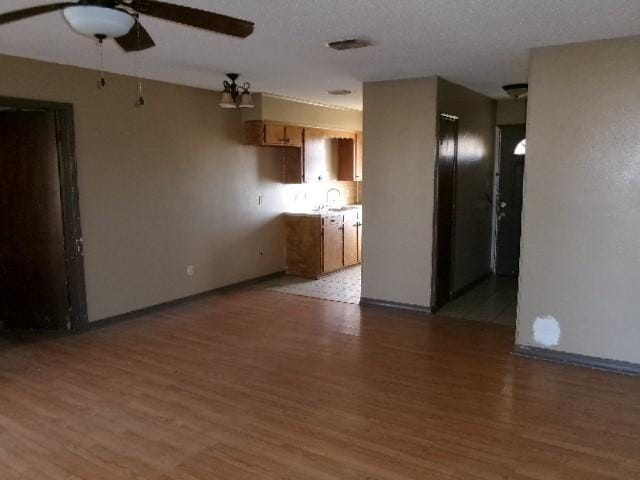 unfurnished living room featuring baseboards, visible vents, a sink, ceiling fan, and light wood-type flooring