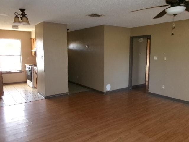 empty room featuring visible vents, baseboards, light wood-style flooring, a textured ceiling, and a ceiling fan