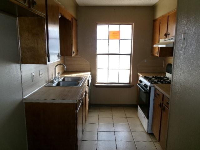 kitchen with light tile patterned floors, a sink, white gas range oven, under cabinet range hood, and tasteful backsplash