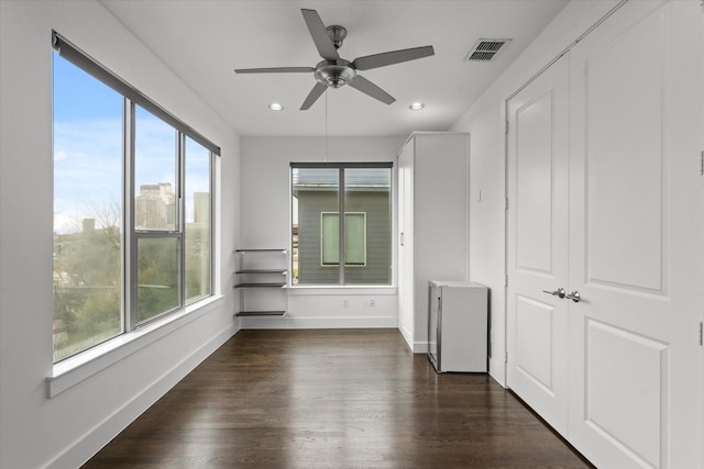 empty room featuring visible vents, plenty of natural light, baseboards, and dark wood-style flooring