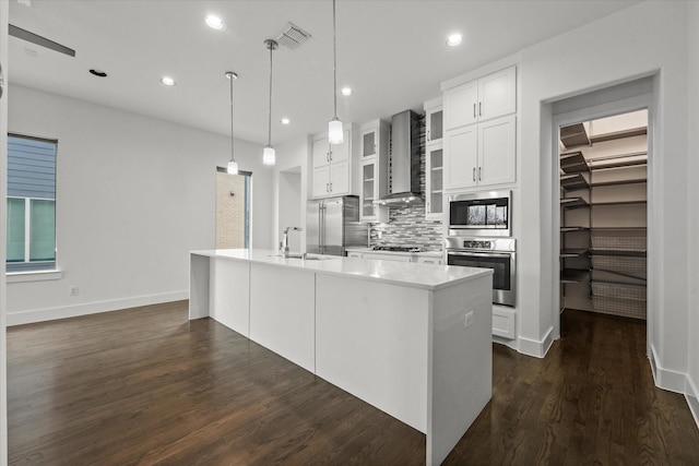 kitchen featuring dark wood-type flooring, an island with sink, appliances with stainless steel finishes, wall chimney exhaust hood, and a sink