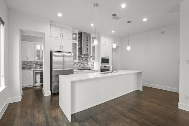 kitchen with beverage cooler, built in appliances, light countertops, wall chimney exhaust hood, and a sink