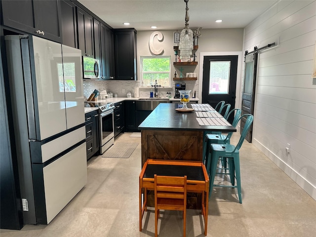 kitchen with tasteful backsplash, dark cabinetry, stainless steel appliances, a barn door, and concrete flooring