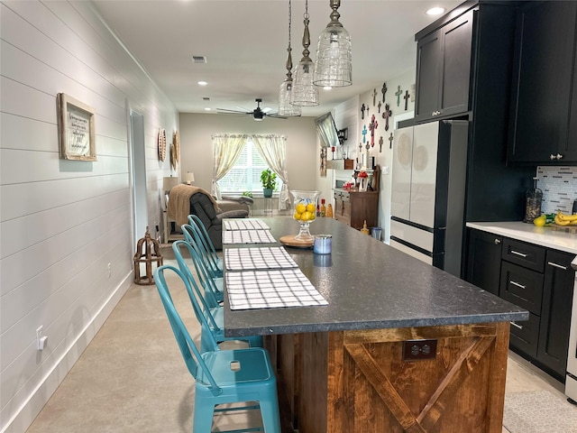 kitchen featuring dark cabinets, freestanding refrigerator, ceiling fan, tasteful backsplash, and open floor plan