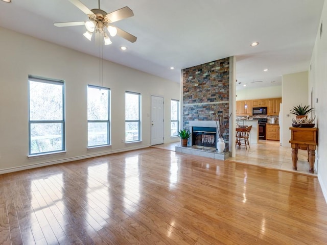 living room with a large fireplace, baseboards, recessed lighting, light wood-style flooring, and a ceiling fan