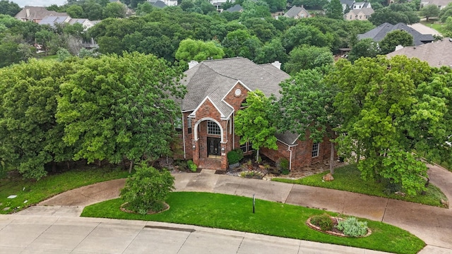 view of front of home with a chimney, roof with shingles, brick siding, curved driveway, and a front lawn